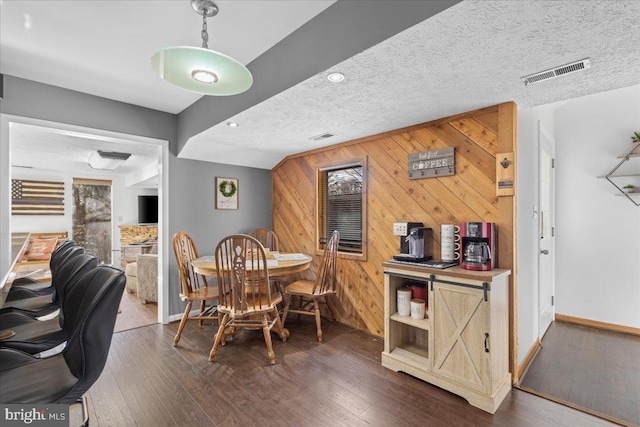 dining area featuring a textured ceiling, hardwood / wood-style floors, visible vents, and wooden walls