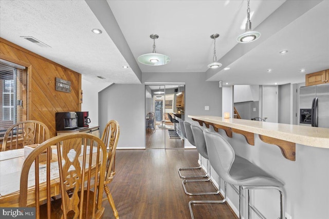 kitchen featuring dark wood finished floors, light countertops, visible vents, hanging light fixtures, and wood walls