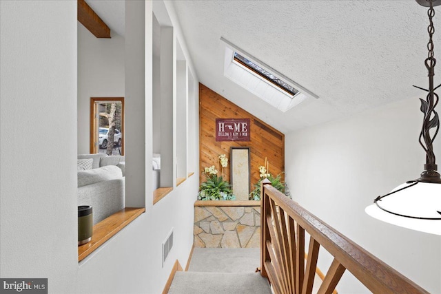 hall featuring a skylight, visible vents, wood walls, a textured ceiling, and an upstairs landing