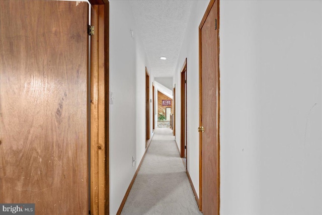 corridor with a textured ceiling, baseboards, and light colored carpet