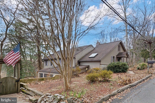 view of side of home with roof with shingles, a chimney, and a gate