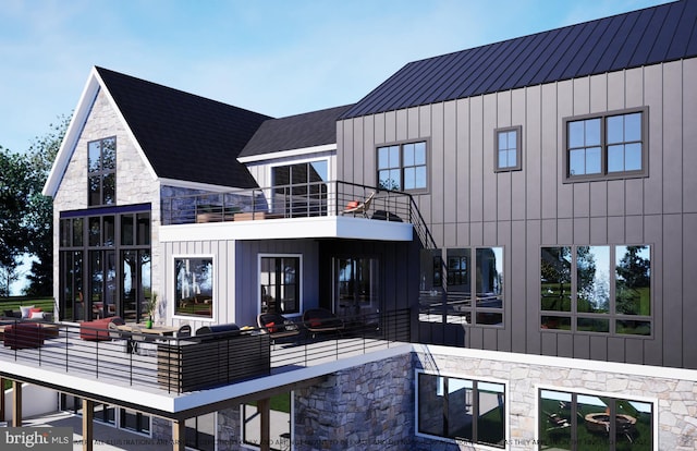 back of property with stone siding, a standing seam roof, board and batten siding, and a balcony