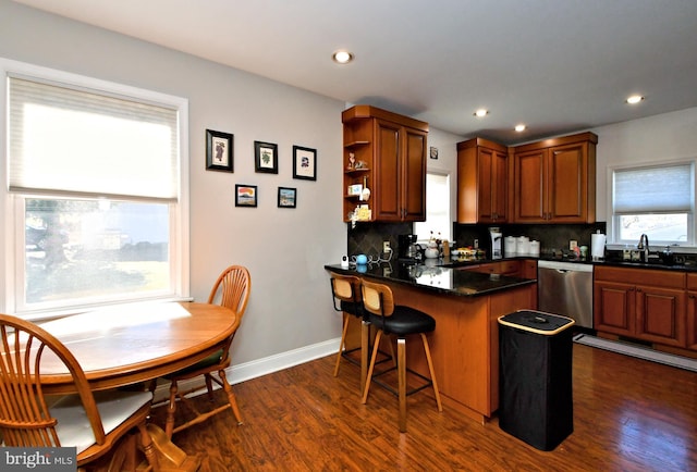 kitchen featuring tasteful backsplash, a peninsula, stainless steel dishwasher, a kitchen bar, and a sink