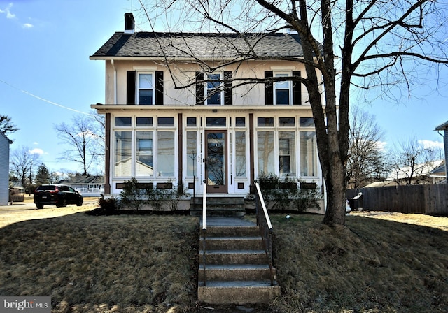 view of front of property with a sunroom, roof with shingles, fence, and a chimney