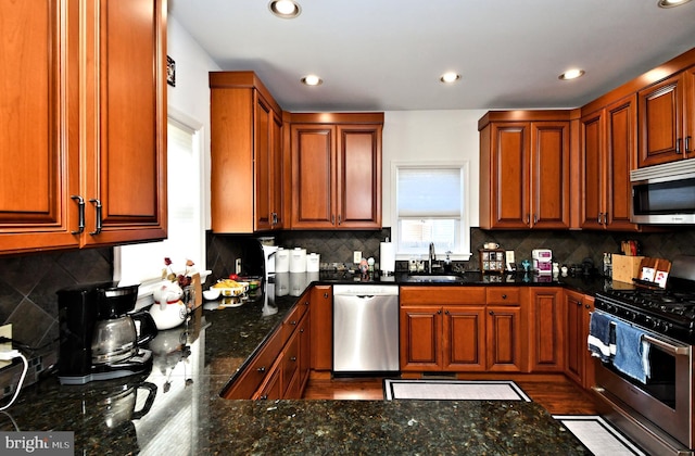 kitchen featuring tasteful backsplash, recessed lighting, appliances with stainless steel finishes, a sink, and dark stone counters