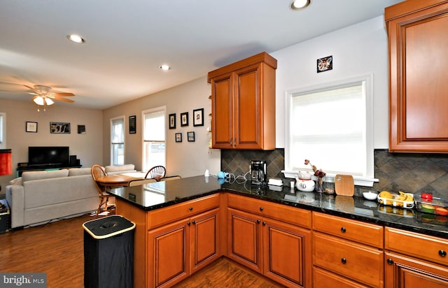 kitchen featuring recessed lighting, a peninsula, brown cabinets, dark countertops, and dark wood finished floors