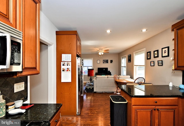 kitchen featuring decorative backsplash, a ceiling fan, appliances with stainless steel finishes, brown cabinets, and dark wood-type flooring