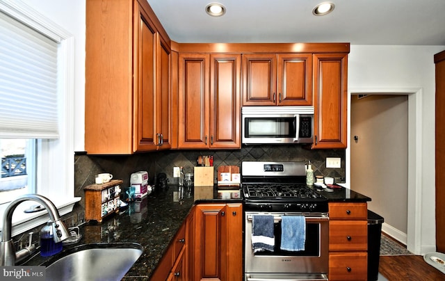 kitchen featuring decorative backsplash, dark stone counters, brown cabinets, stainless steel appliances, and a sink