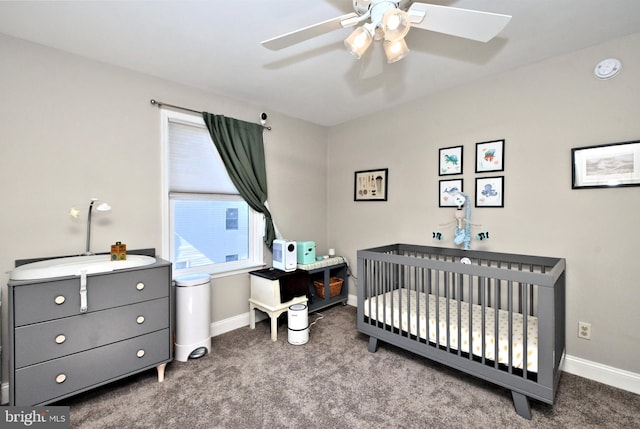 carpeted bedroom with a crib, ceiling fan, and baseboards