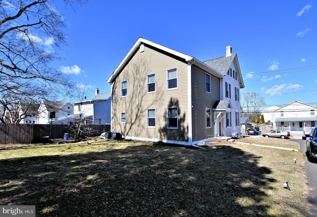 view of side of home with a chimney, fence, and a lawn