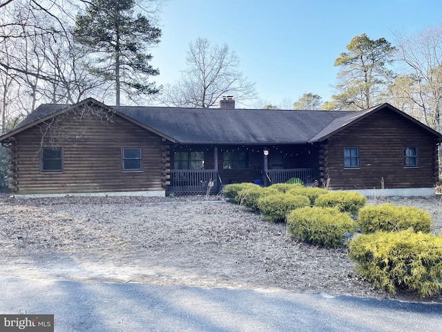 cabin featuring a porch, a chimney, and log siding