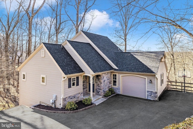 view of front of home featuring aphalt driveway, stone siding, roof with shingles, and an attached garage