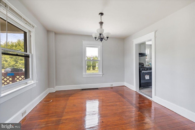 unfurnished room featuring baseboards, visible vents, hardwood / wood-style flooring, and a notable chandelier