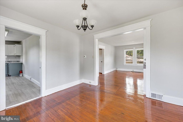 unfurnished dining area featuring baseboards, wood-type flooring, visible vents, and a notable chandelier