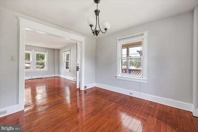 unfurnished room with wood-type flooring, a notable chandelier, and baseboards