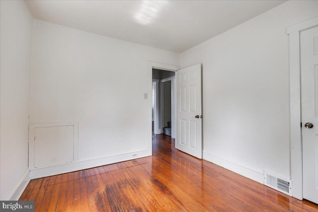 spare room with wood-type flooring, visible vents, and baseboards