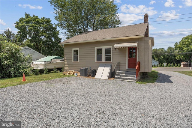 back of property with roof with shingles, a chimney, gravel driveway, and central air condition unit