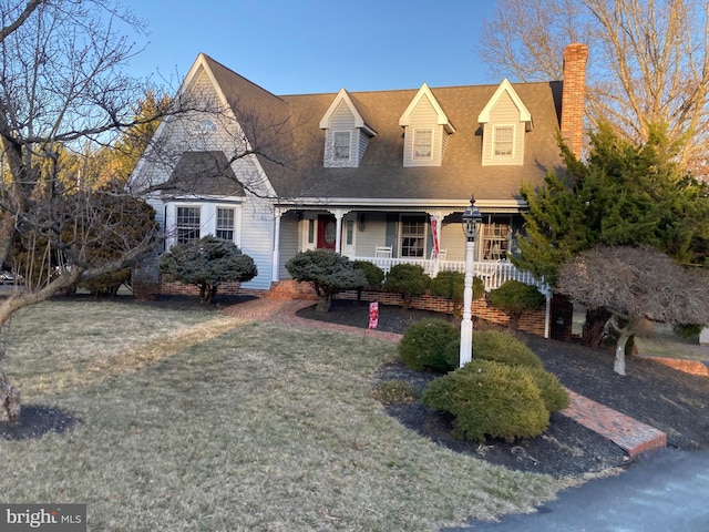 view of front of home featuring covered porch, a chimney, and a front yard