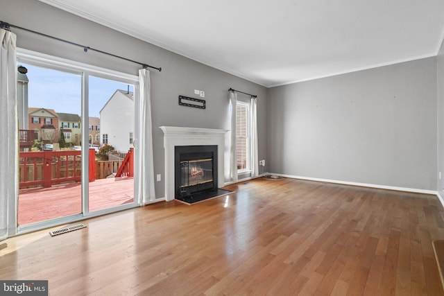 unfurnished living room featuring visible vents, ornamental molding, a fireplace with flush hearth, and wood finished floors