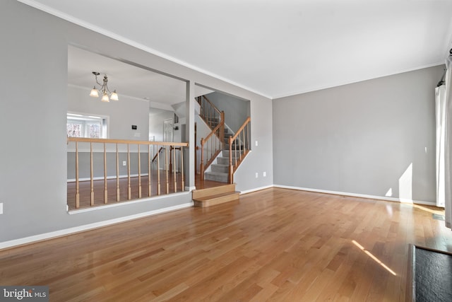 empty room with a chandelier, crown molding, stairs, and wood finished floors