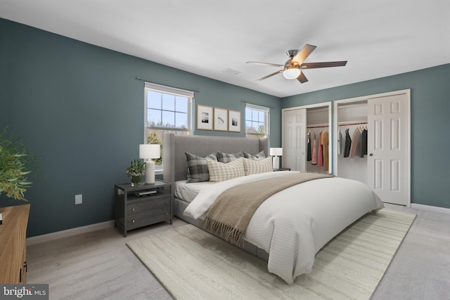 bedroom with visible vents, light carpet, two closets, baseboards, and ceiling fan