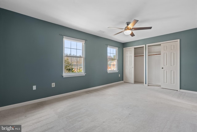 unfurnished bedroom with ceiling fan, two closets, baseboards, and carpet floors