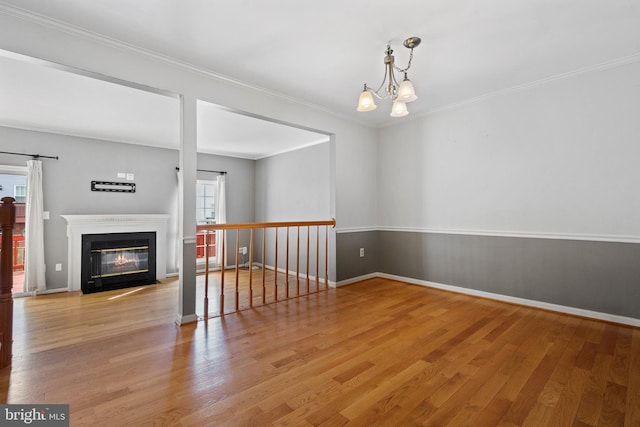 spare room with crown molding, a chandelier, a fireplace with flush hearth, a barn door, and wood finished floors