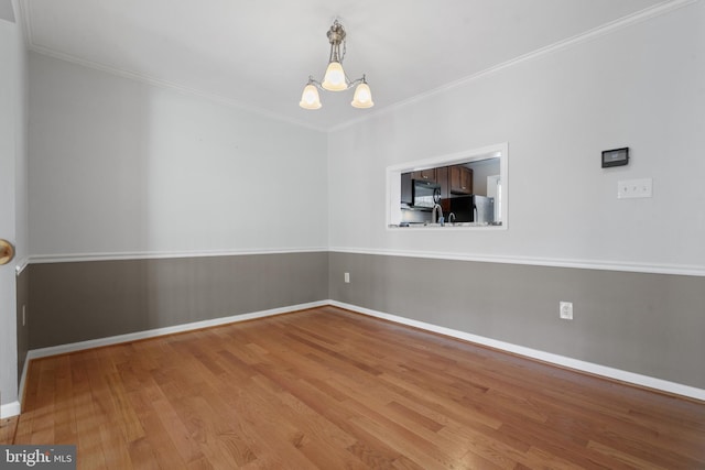 empty room with baseboards, wood finished floors, a chandelier, and ornamental molding