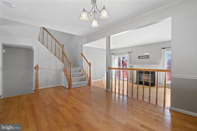 unfurnished room featuring a notable chandelier, stairway, a glass covered fireplace, and wood finished floors