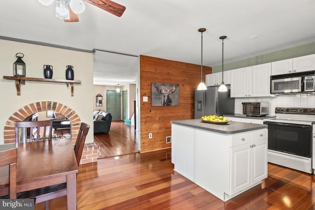 kitchen with backsplash, wood walls, appliances with stainless steel finishes, wood finished floors, and white cabinets