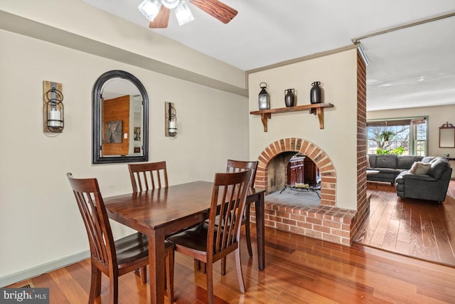 dining area with wood-type flooring, a brick fireplace, and ceiling fan