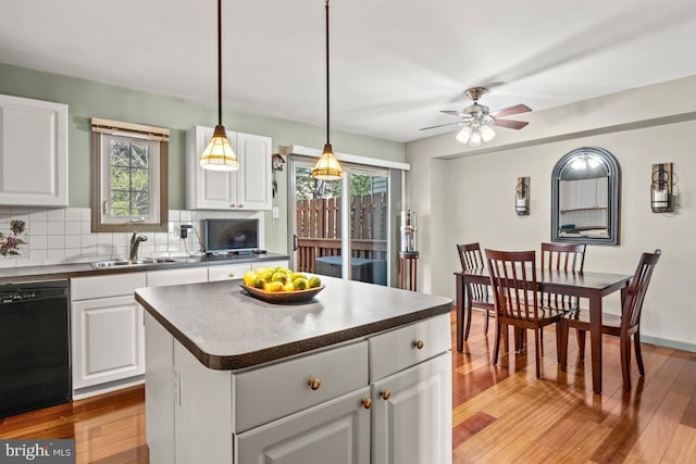 kitchen with a sink, black dishwasher, dark countertops, light wood-type flooring, and backsplash