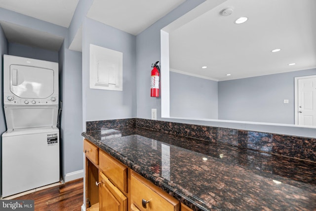 kitchen with dark wood-style floors, recessed lighting, stacked washing maching and dryer, dark stone counters, and baseboards