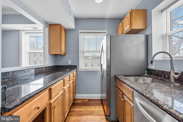 kitchen with stainless steel appliances, a sink, baseboards, light wood-style floors, and dark stone countertops