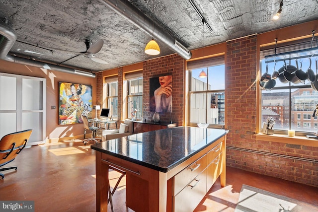 kitchen featuring dark stone countertops, a ceiling fan, brick wall, a kitchen island, and finished concrete floors