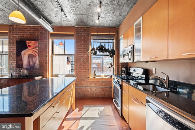 kitchen with brick wall, dark stone counters, a sink, stainless steel appliances, and rail lighting