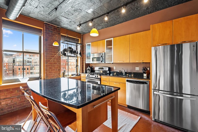 kitchen with dark stone countertops, a kitchen island, concrete floors, appliances with stainless steel finishes, and brick wall