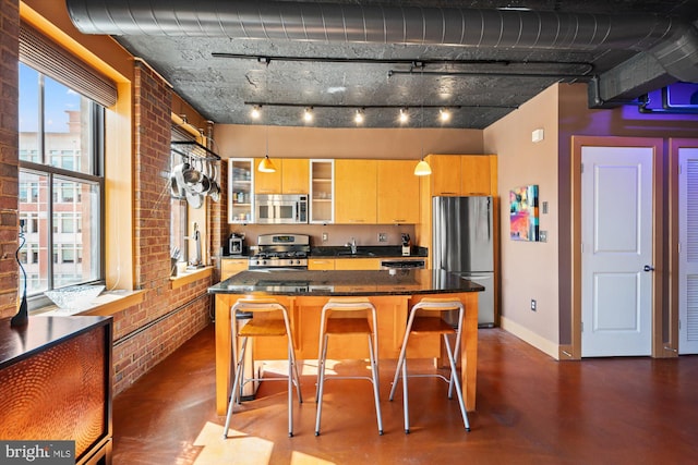 kitchen featuring brick wall, a center island, baseboards, a breakfast bar, and stainless steel appliances