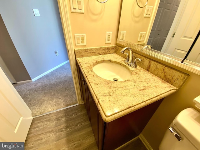 half bath featuring wood finished floors, vanity, toilet, and baseboards