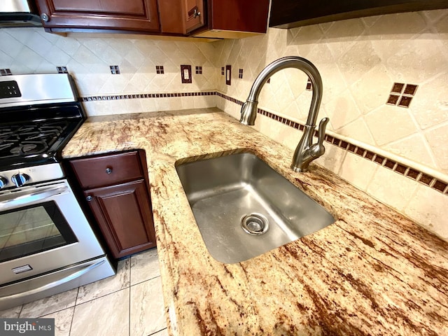 kitchen with light stone countertops, tasteful backsplash, stainless steel range with gas cooktop, and a sink