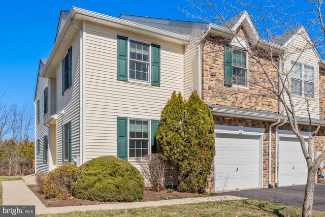 townhome / multi-family property featuring stone siding, driveway, and a garage