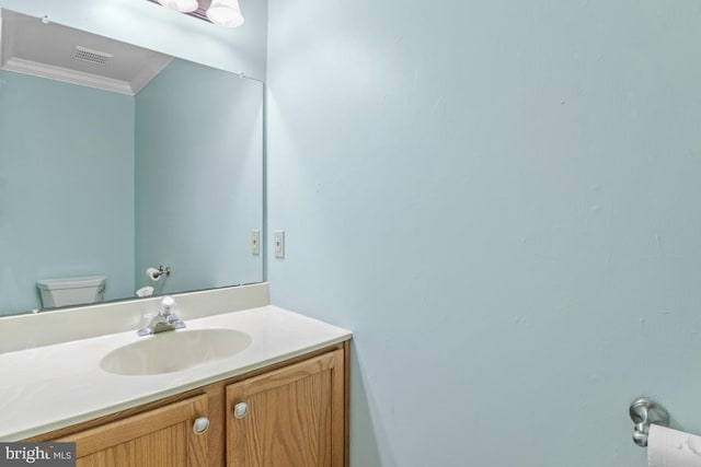 half bath with vanity, crown molding, toilet, and visible vents