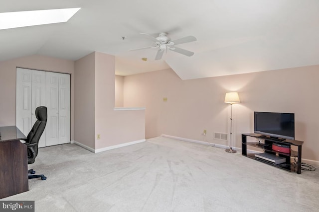 carpeted office with a ceiling fan, vaulted ceiling with skylight, baseboards, and visible vents