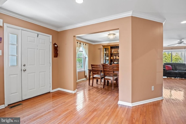 entryway featuring light wood-type flooring, visible vents, ornamental molding, a ceiling fan, and baseboards