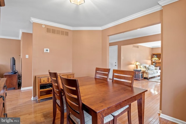 dining space with visible vents, light wood-style flooring, crown molding, and baseboards