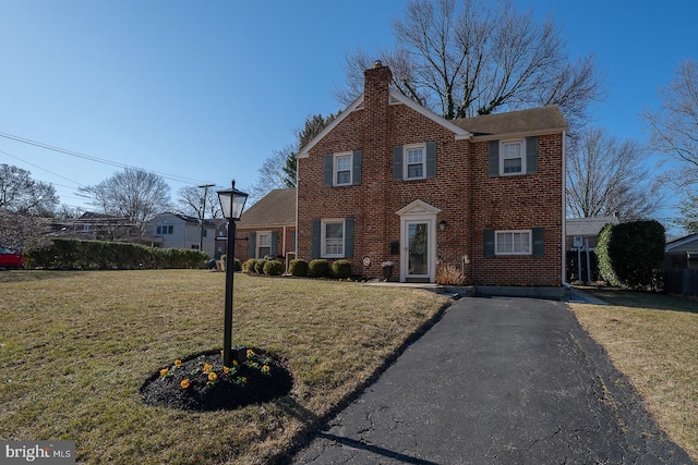 view of front of home featuring brick siding, a chimney, and a front lawn