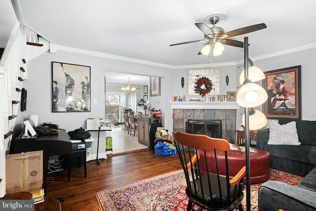 living area featuring ornamental molding, ceiling fan with notable chandelier, a fireplace, and wood finished floors