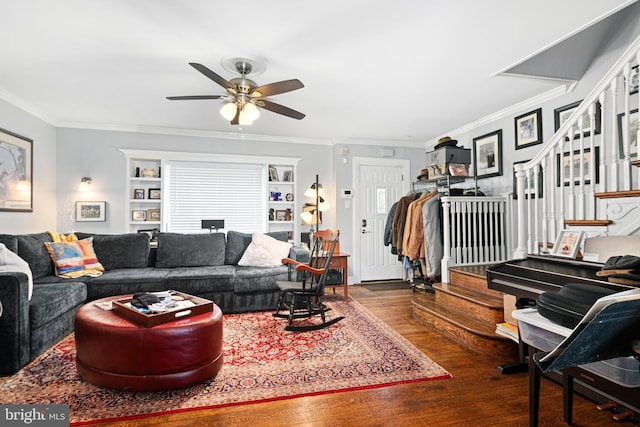 living area with ceiling fan, wood finished floors, crown molding, and stairs