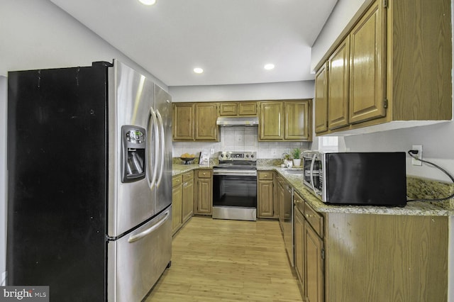 kitchen with light wood finished floors, tasteful backsplash, under cabinet range hood, appliances with stainless steel finishes, and brown cabinetry