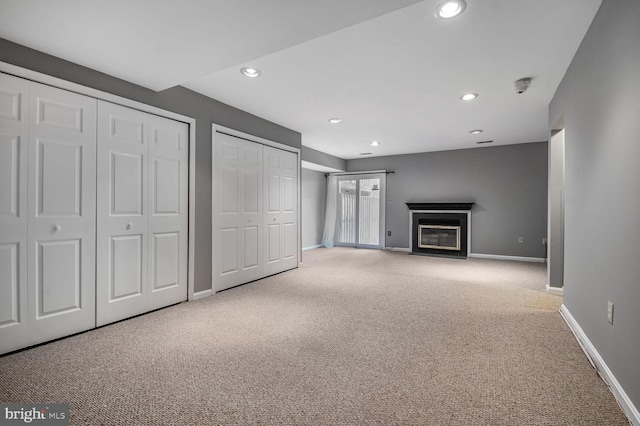 unfurnished living room featuring a fireplace with flush hearth, recessed lighting, baseboards, and carpet floors